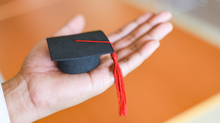 miniatura de chapéu de graduação na palma de uma pessoa branca.