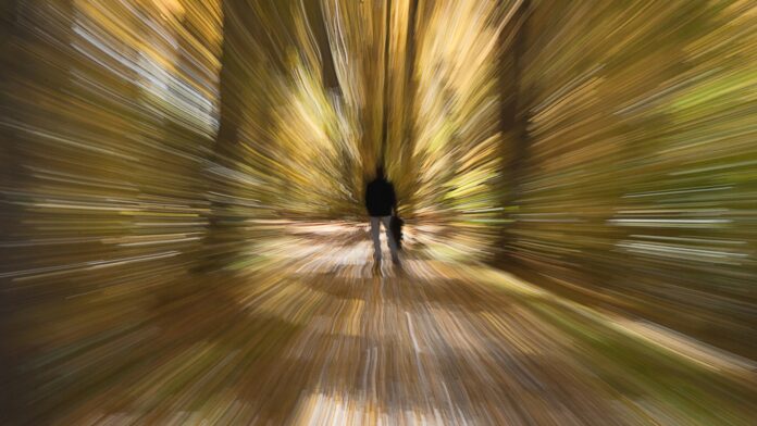 Imagem artisticamente distorcida que simula vertigem ou tontura, mostrando um homem de costas em uma trilha florestal, com o fundo em efeito de movimento radial.