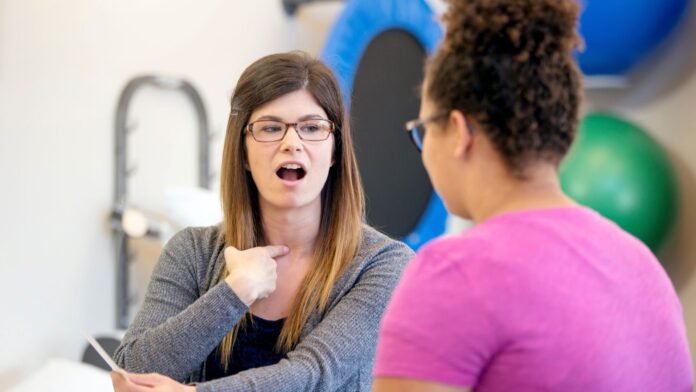 foniatria Terapeuta realizando uma sessão de fonoaudiologia com uma paciente, demonstrando movimentos vocais.