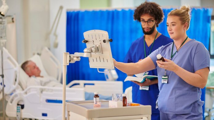 especialidades acesso direto Profissionais de saúde verificando informações em um monitor e manuseando medicações, com um paciente deitado em uma cama hospitalar ao fundo.